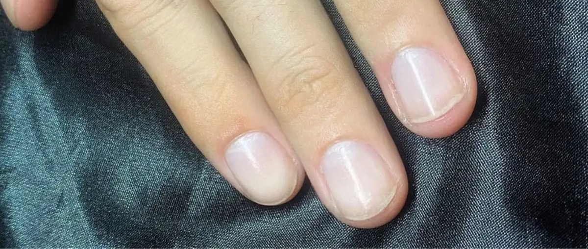Close-up of a hand with light pink nail polish on a dark fabric background